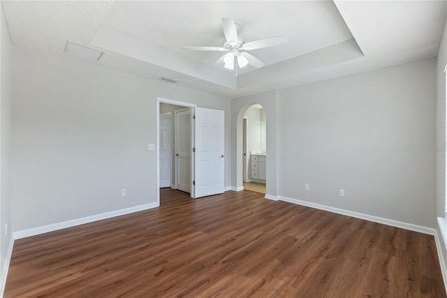 unfurnished bedroom with ceiling fan, dark hardwood / wood-style floors, and a raised ceiling