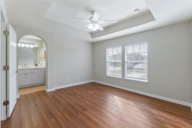 unfurnished bedroom with sink, a textured ceiling, dark hardwood / wood-style flooring, and a tray ceiling