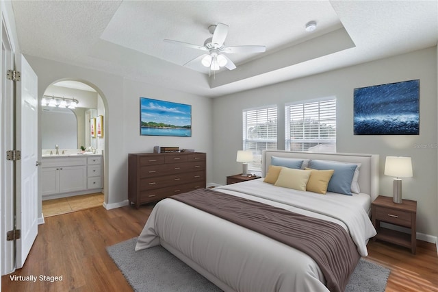 bedroom with dark hardwood / wood-style floors, connected bathroom, sink, a tray ceiling, and a textured ceiling