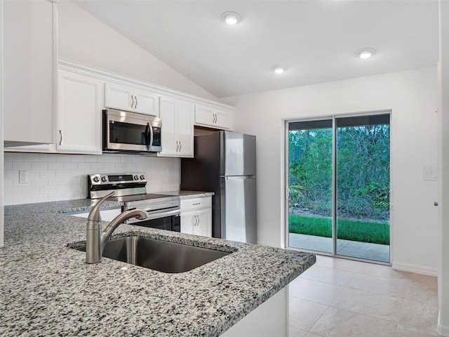 kitchen featuring light stone countertops, white cabinets, appliances with stainless steel finishes, lofted ceiling, and sink