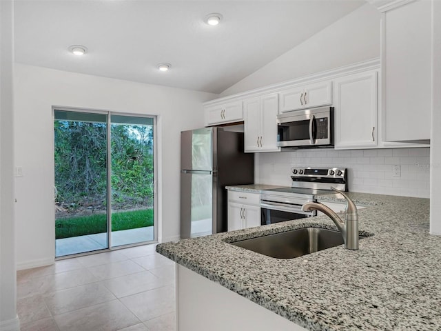 kitchen featuring white cabinetry, appliances with stainless steel finishes, vaulted ceiling, light stone counters, and sink