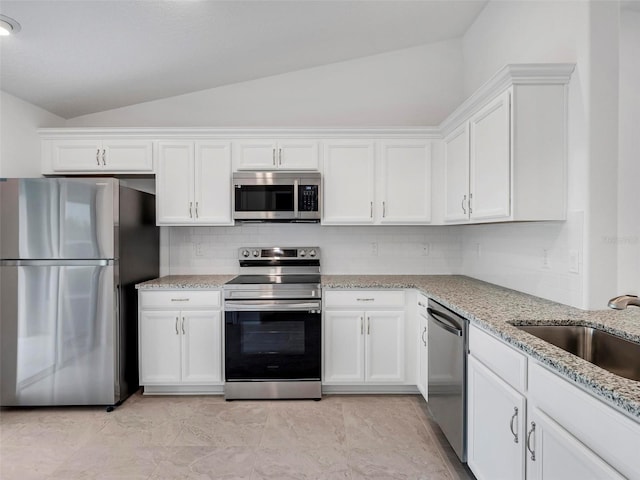 kitchen with light stone countertops, appliances with stainless steel finishes, lofted ceiling, white cabinetry, and sink