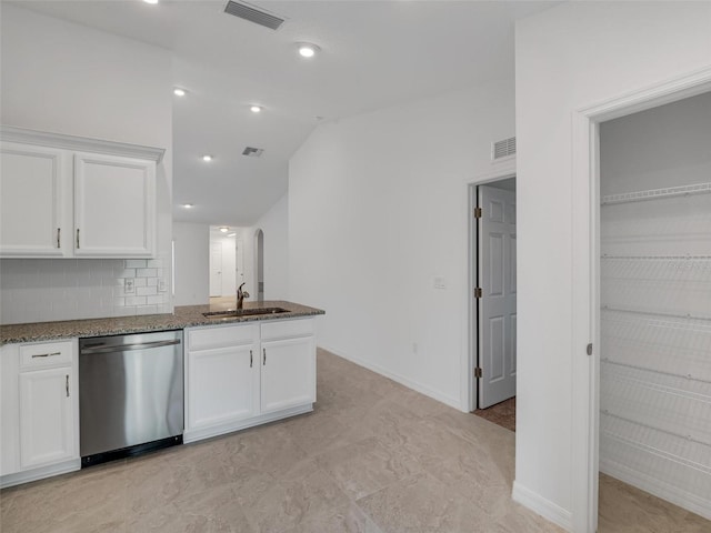 kitchen with white cabinetry, tasteful backsplash, dark stone countertops, stainless steel dishwasher, and sink