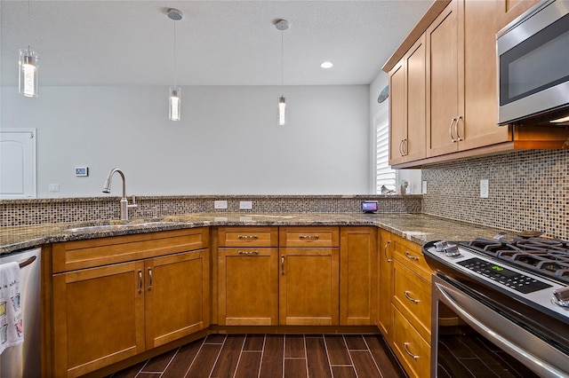 kitchen featuring appliances with stainless steel finishes, decorative light fixtures, dark stone counters, tasteful backsplash, and sink