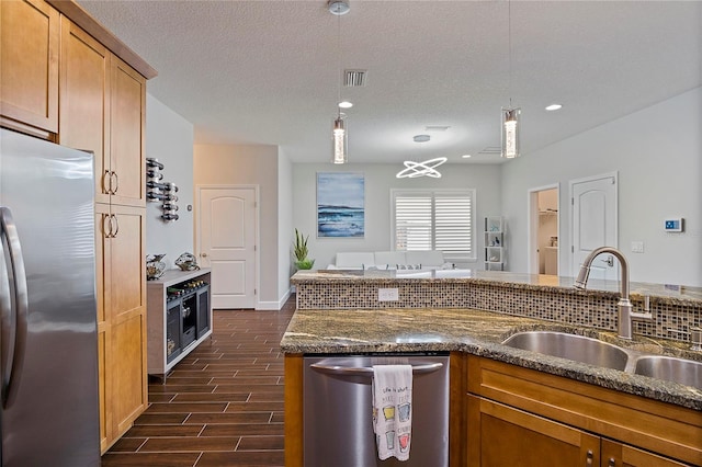 kitchen with decorative light fixtures, sink, appliances with stainless steel finishes, a textured ceiling, and dark stone counters