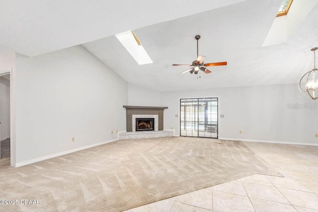 unfurnished living room featuring light carpet, vaulted ceiling with skylight, a fireplace, and ceiling fan with notable chandelier