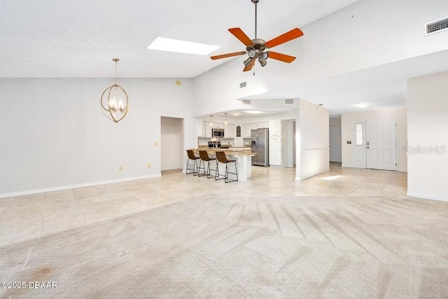 unfurnished living room with lofted ceiling with skylight, light tile patterned flooring, and ceiling fan with notable chandelier