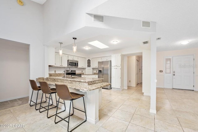 kitchen featuring a kitchen bar, kitchen peninsula, stainless steel appliances, light stone countertops, and white cabinets