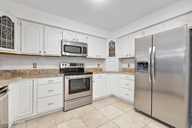 kitchen with light stone countertops, white cabinetry, stainless steel appliances, backsplash, and light tile patterned floors