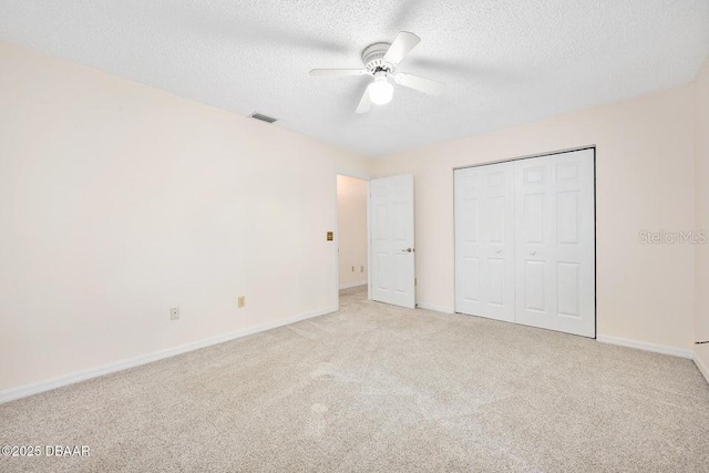 unfurnished bedroom with ceiling fan, light colored carpet, a closet, and a textured ceiling