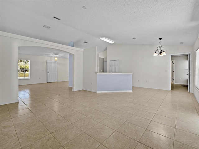 empty room with a textured ceiling, light tile patterned floors, lofted ceiling, and a chandelier