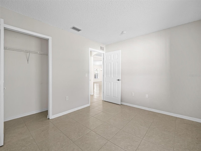 unfurnished bedroom featuring a textured ceiling, light tile patterned floors, and a closet