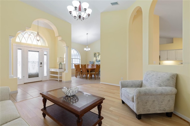 living room featuring light hardwood / wood-style floors, high vaulted ceiling, decorative columns, and a notable chandelier