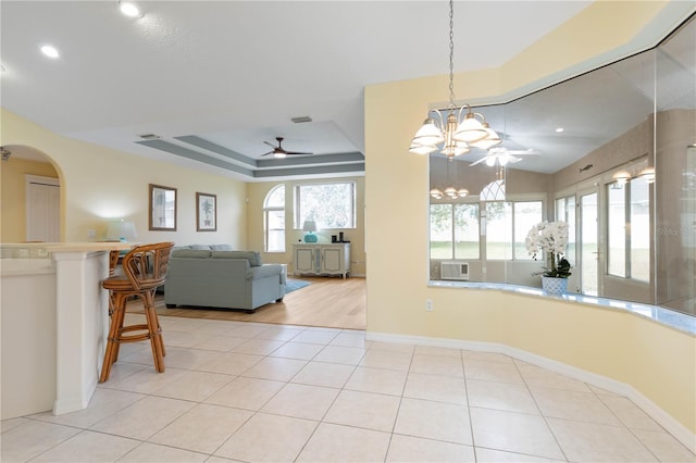 tiled dining area with ceiling fan with notable chandelier and a tray ceiling