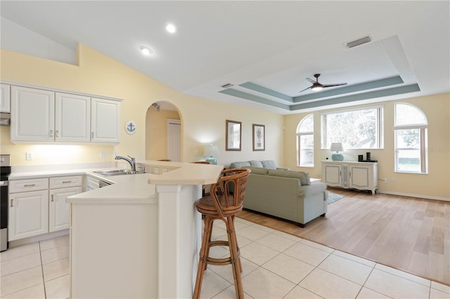 kitchen with light tile patterned floors, ceiling fan, a breakfast bar area, white cabinets, and sink