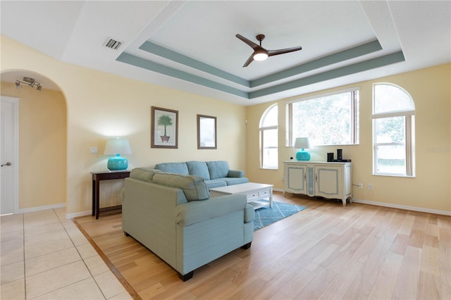 living room with a raised ceiling, light wood-type flooring, and ceiling fan