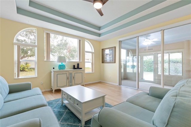 living room with ceiling fan, light hardwood / wood-style floors, and a tray ceiling