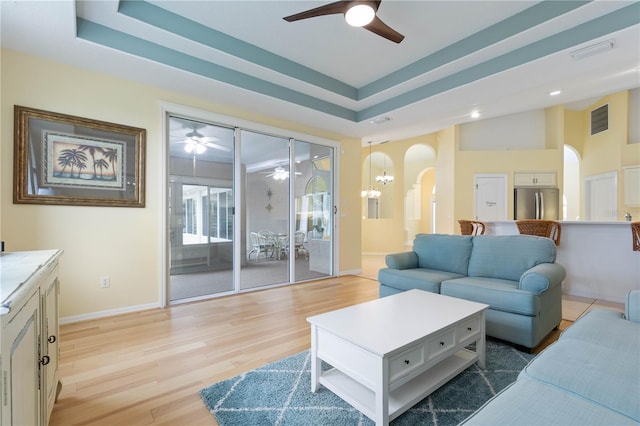 living room featuring light hardwood / wood-style floors, a raised ceiling, and ceiling fan