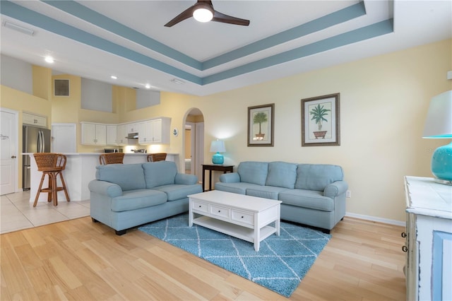 living room with ceiling fan, light hardwood / wood-style floors, and a raised ceiling