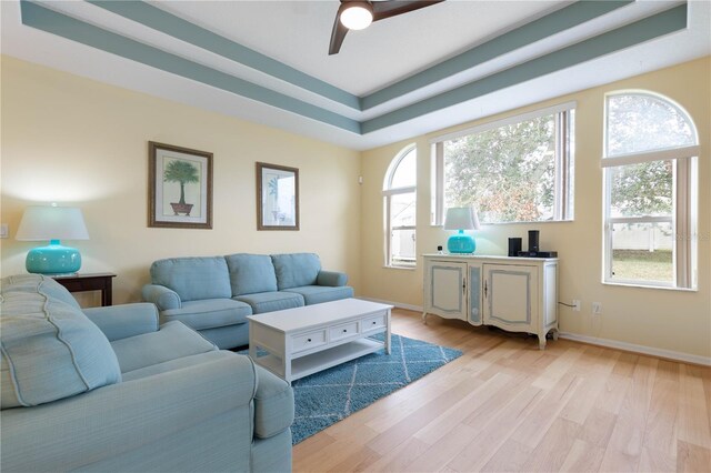 living room featuring ceiling fan, plenty of natural light, light hardwood / wood-style flooring, and a raised ceiling