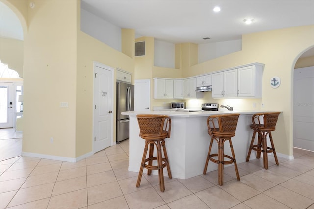 kitchen featuring white cabinets, appliances with stainless steel finishes, kitchen peninsula, light tile patterned flooring, and a breakfast bar