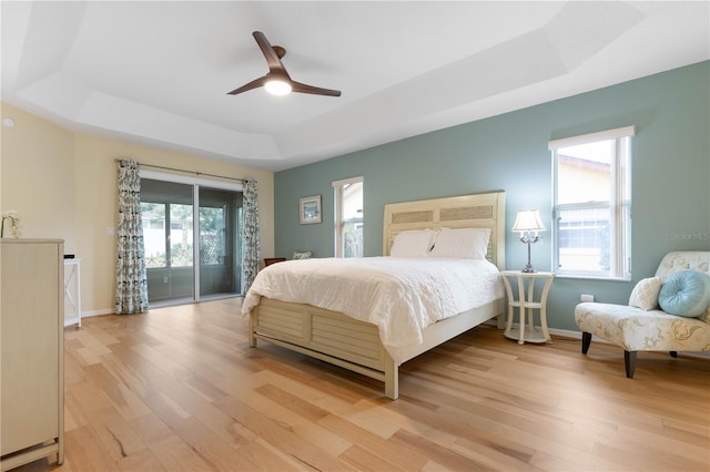 bedroom with light wood-type flooring, ceiling fan, a raised ceiling, and access to outside