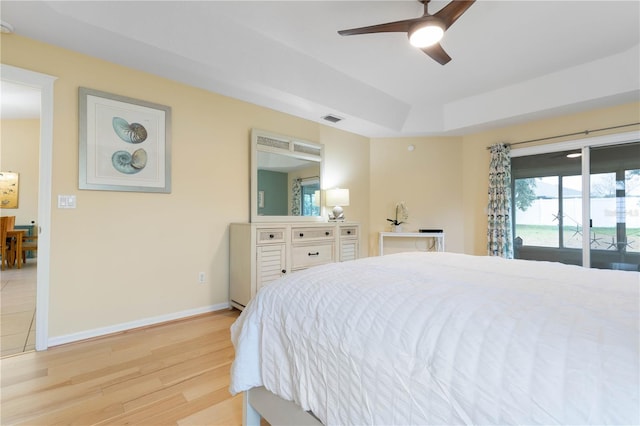 bedroom featuring access to outside, ceiling fan, a tray ceiling, and light hardwood / wood-style flooring