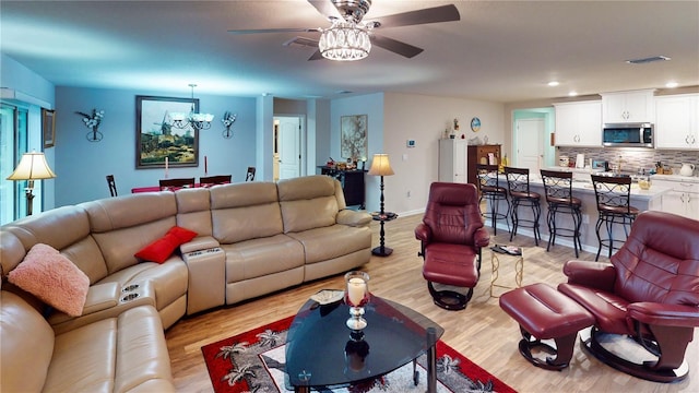 living room featuring ceiling fan with notable chandelier and light hardwood / wood-style flooring