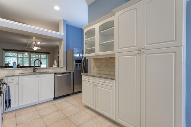 kitchen featuring light stone countertops, white cabinets, stainless steel appliances, decorative backsplash, and sink