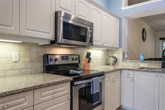 kitchen featuring tasteful backsplash, white cabinets, appliances with stainless steel finishes, and sink