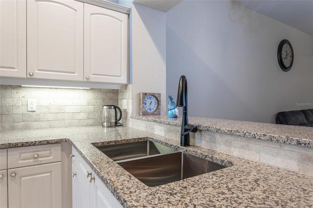 kitchen with decorative backsplash, sink, white cabinets, and light stone countertops