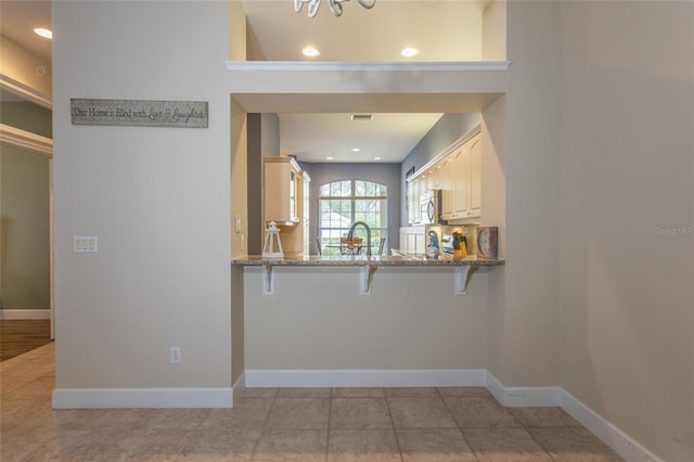 kitchen with kitchen peninsula, a kitchen breakfast bar, light tile patterned flooring, light stone countertops, and sink