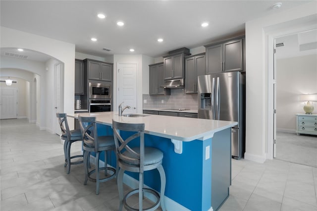 kitchen featuring backsplash, a center island with sink, sink, a kitchen breakfast bar, and stainless steel appliances