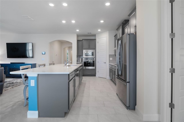 kitchen with appliances with stainless steel finishes, a kitchen bar, sink, gray cabinets, and a center island with sink