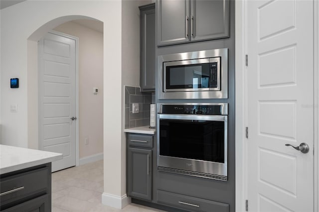 kitchen featuring backsplash, gray cabinets, light tile patterned flooring, appliances with stainless steel finishes, and light stone counters