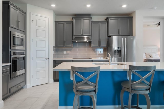 kitchen featuring backsplash, gray cabinets, a kitchen bar, sink, and stainless steel appliances