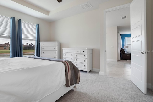 bedroom with ceiling fan, light colored carpet, and a tray ceiling