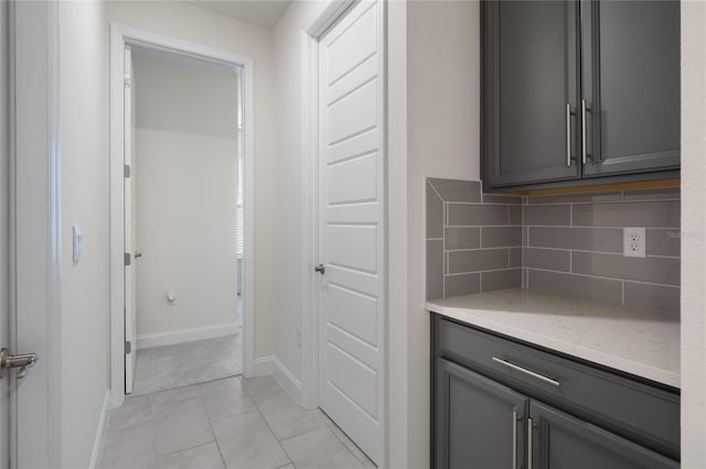 interior space featuring light tile patterned floors, decorative backsplash, light stone countertops, and gray cabinetry