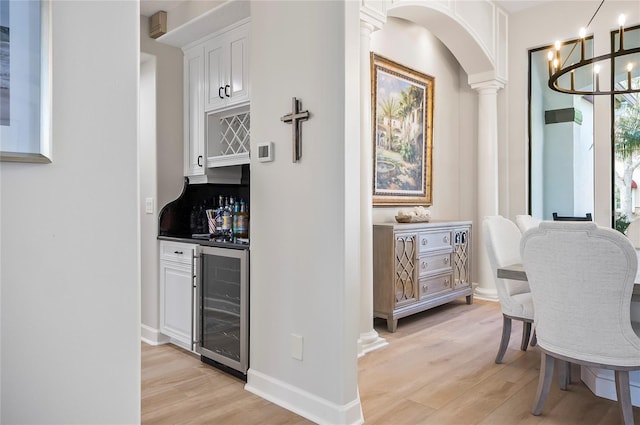 interior space featuring white cabinets, tasteful backsplash, wine cooler, decorative columns, and light hardwood / wood-style flooring