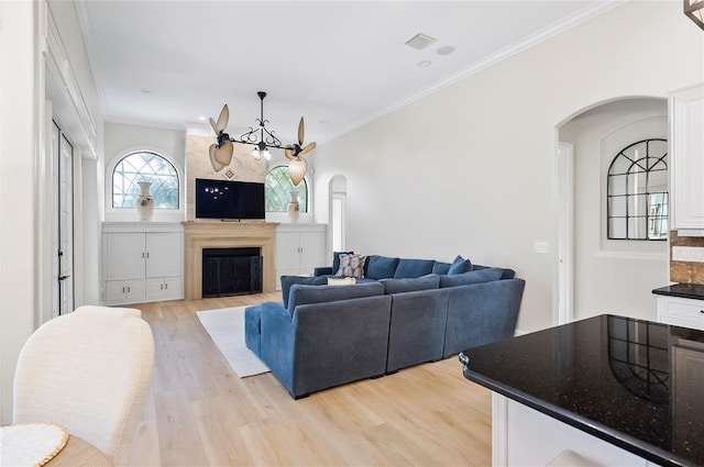 living room featuring a chandelier, light hardwood / wood-style flooring, a large fireplace, and ornamental molding