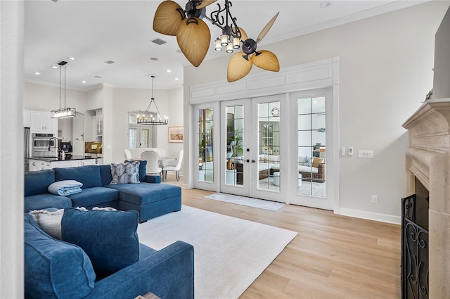 living room with ceiling fan with notable chandelier, light hardwood / wood-style floors, ornamental molding, and french doors