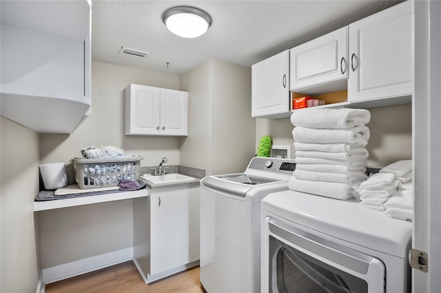 laundry area featuring light wood-type flooring, separate washer and dryer, a textured ceiling, cabinets, and sink