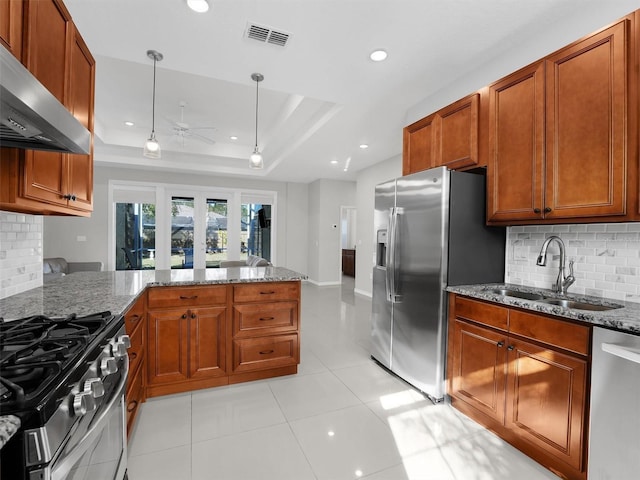 kitchen featuring pendant lighting, sink, stainless steel appliances, a raised ceiling, and wall chimney exhaust hood