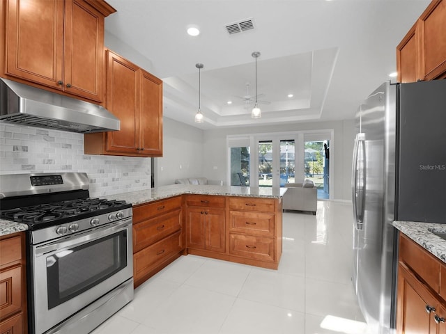 kitchen featuring a raised ceiling, backsplash, light stone counters, kitchen peninsula, and stainless steel appliances