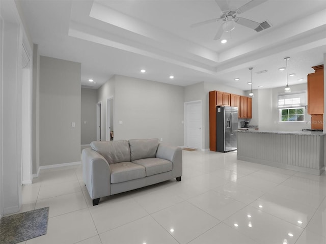 living room with light tile patterned flooring, ceiling fan, and a raised ceiling