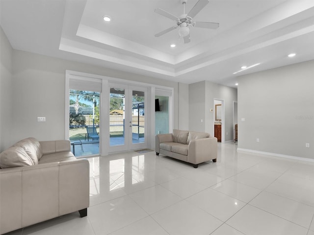 living room with a tray ceiling, light tile patterned floors, ceiling fan, and french doors