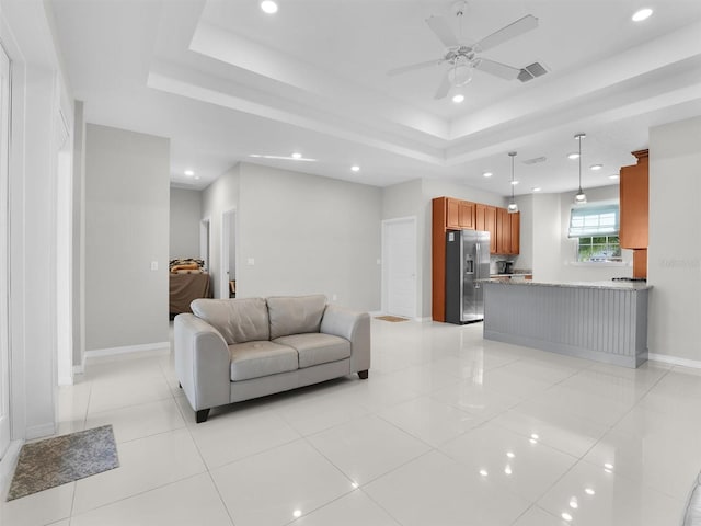 living room with light tile patterned floors, a raised ceiling, and ceiling fan