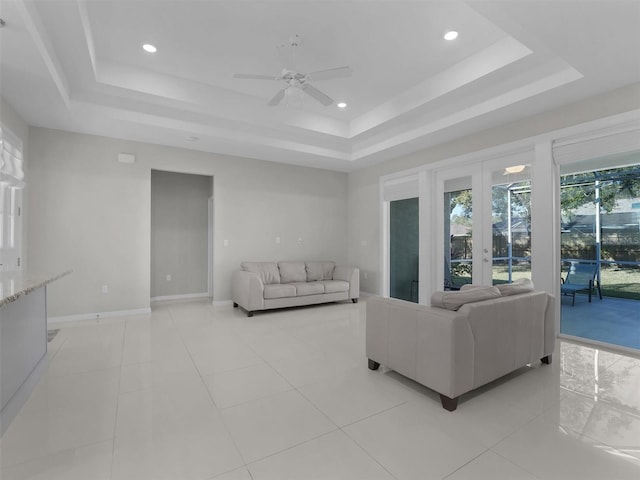 tiled living room featuring a tray ceiling, french doors, and ceiling fan