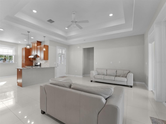 tiled living room with a raised ceiling and ceiling fan