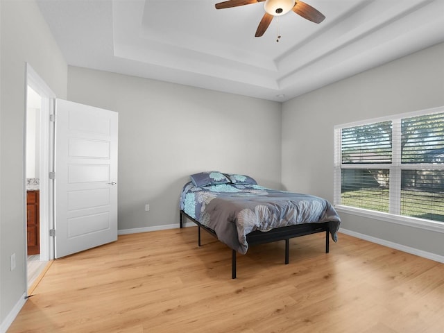 bedroom with light hardwood / wood-style flooring, a raised ceiling, and ceiling fan